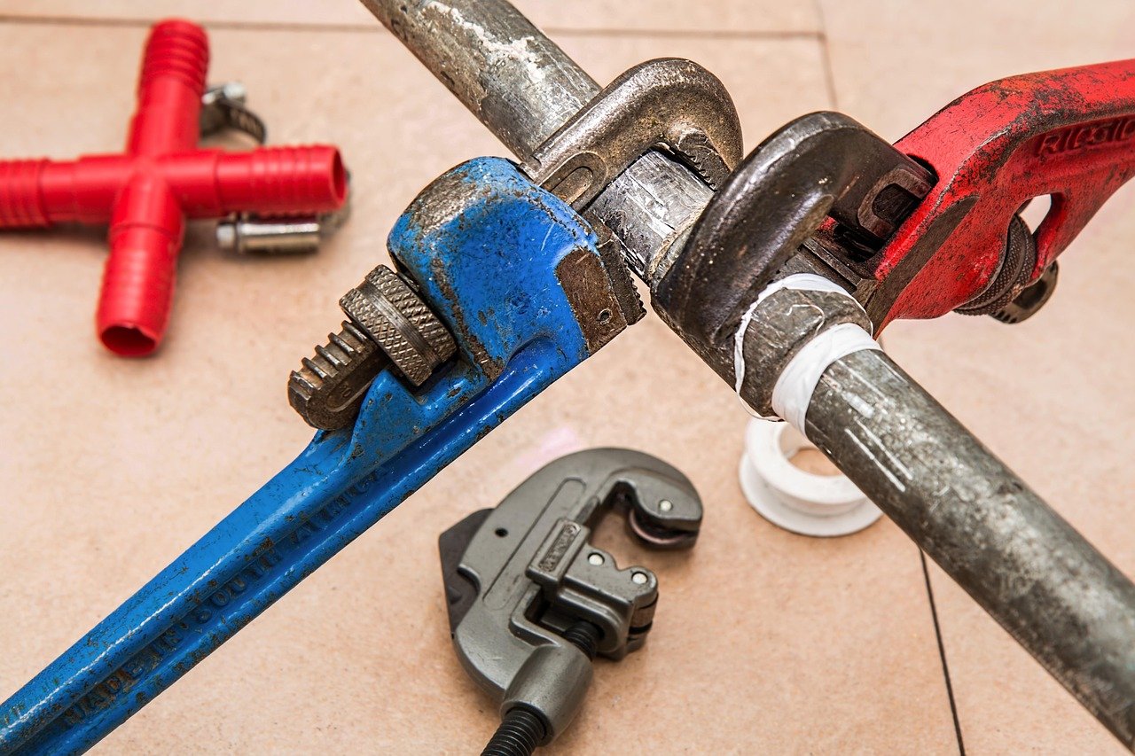 Pipe wrenches, a pipe cutter and fittings laid out on a tiled floor