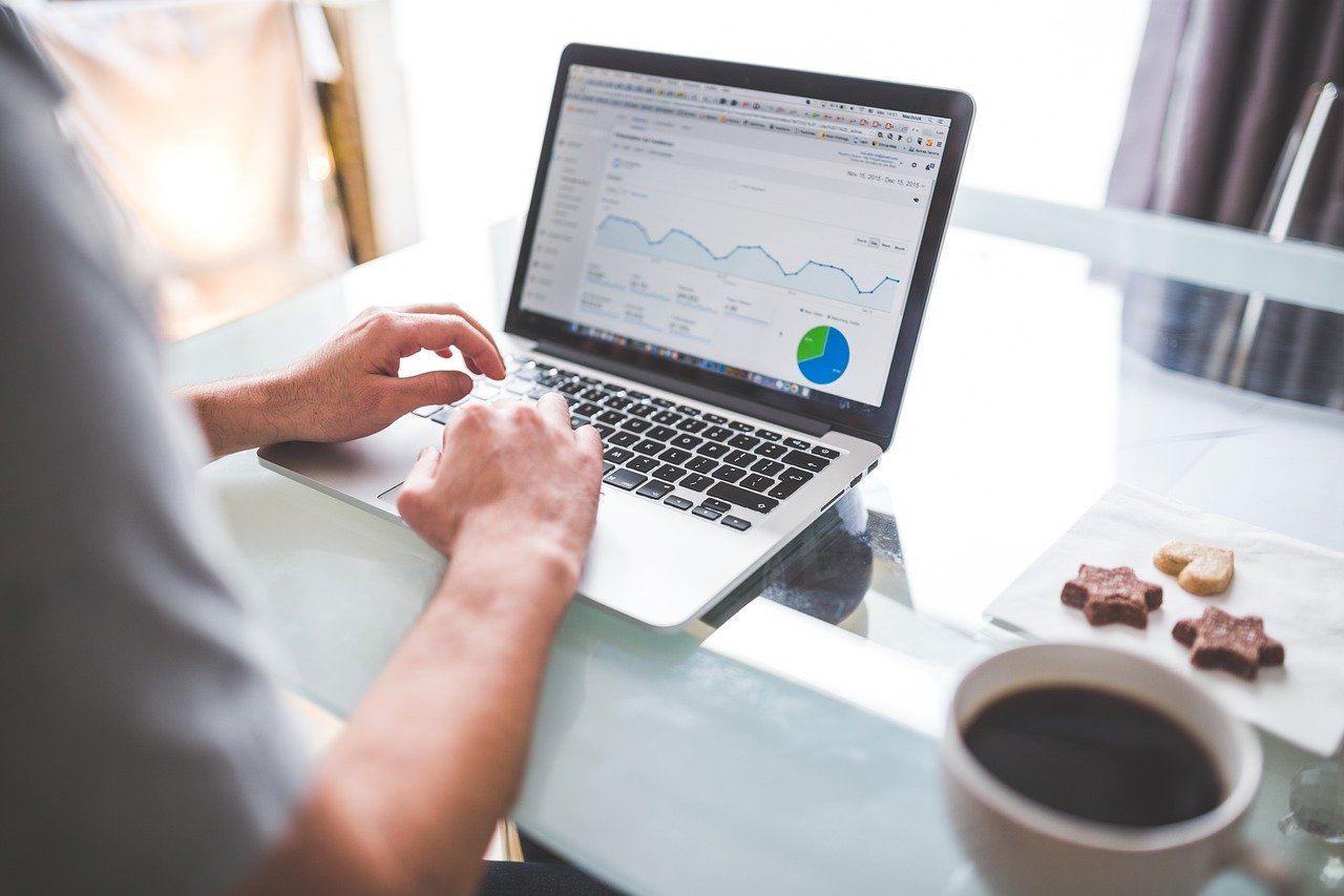 Man typing on a laptop showing an analytics dashboard with a line trend chart and a blue and green pie chart