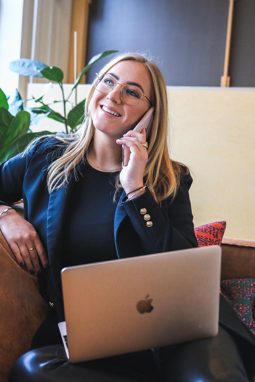 Smiling woman in a blazer and glasses taking an enquiry call with her laptop open on her lap