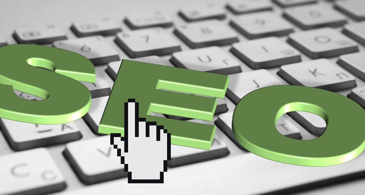 Three-dimensional green letters spelling SEO resting on a white keyboard beside a hand-shaped cursor