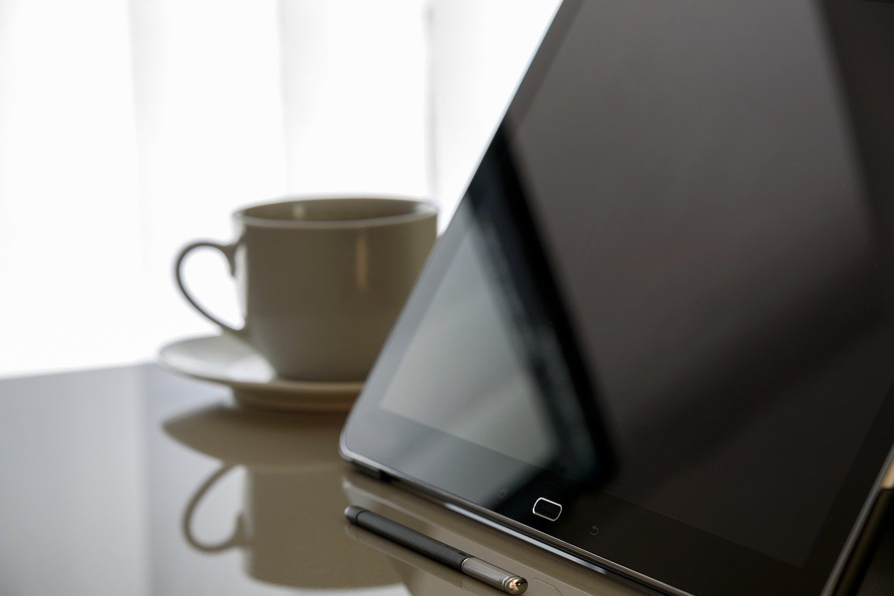 Tablet propped upright on a glossy desk beside a stylus and an empty cup and saucer, its screen dark and blank